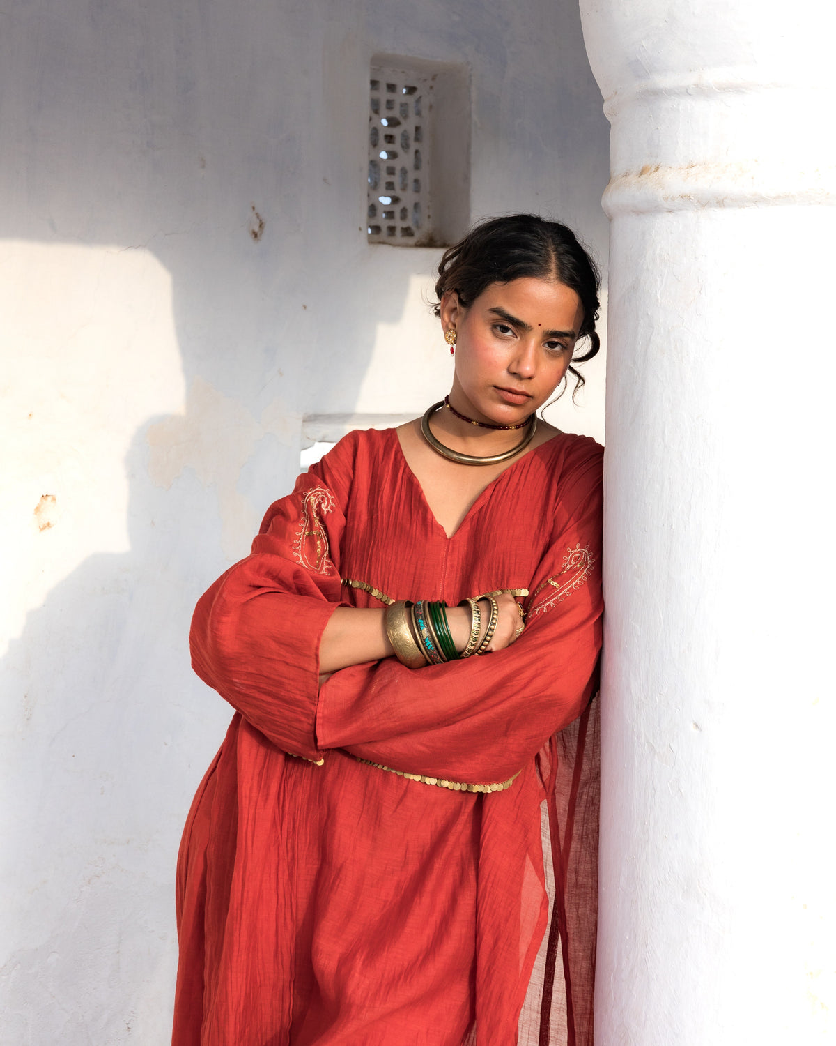 A woman wearing a rust-red modified kalidar kurta and multiple gold-toned bangles.